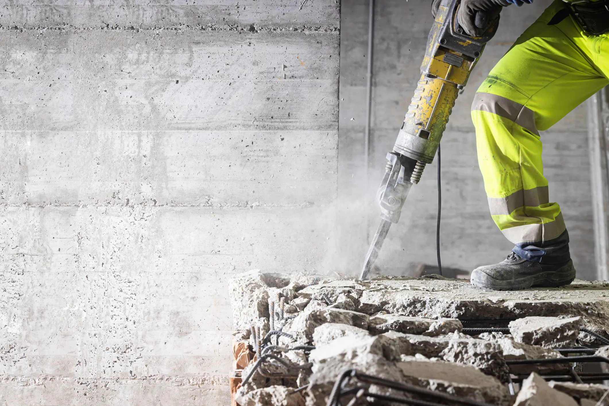 A person in yellow jacket using a hammer on concrete.